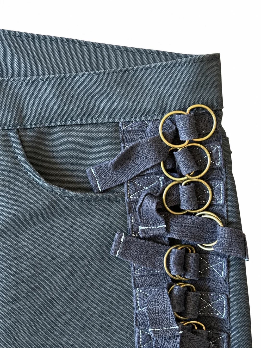 Close-up of waxed denim, cotton bondage straps, and brass rings.